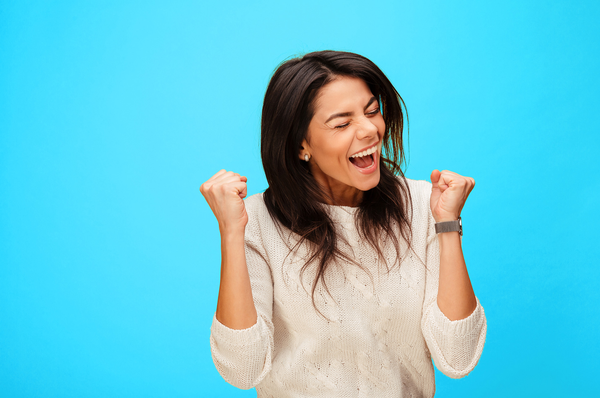 Woman with dark hair smiles and cheers in front of a bright blue background.
